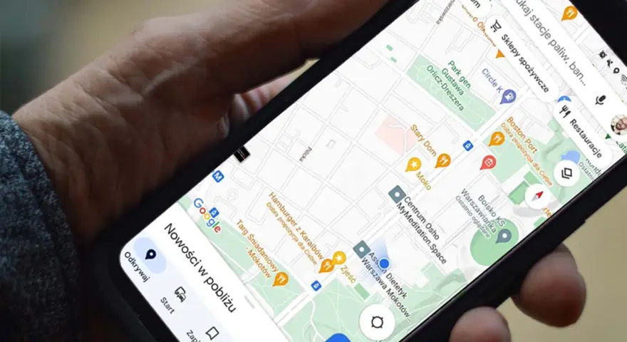 Dłoń trzyma telefon z mapą. Aplikacja do udostępniania lokalizacji pokazuje pobliskie restauracje i sklepy.