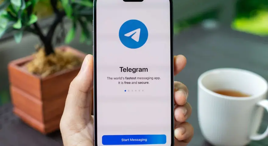 Dłoń trzyma smartfon z otwartą aplikacją Telegram. Na ekranie widnieje logo i napis "Telegram. The world's fastest messaging app. It is free and secure.
