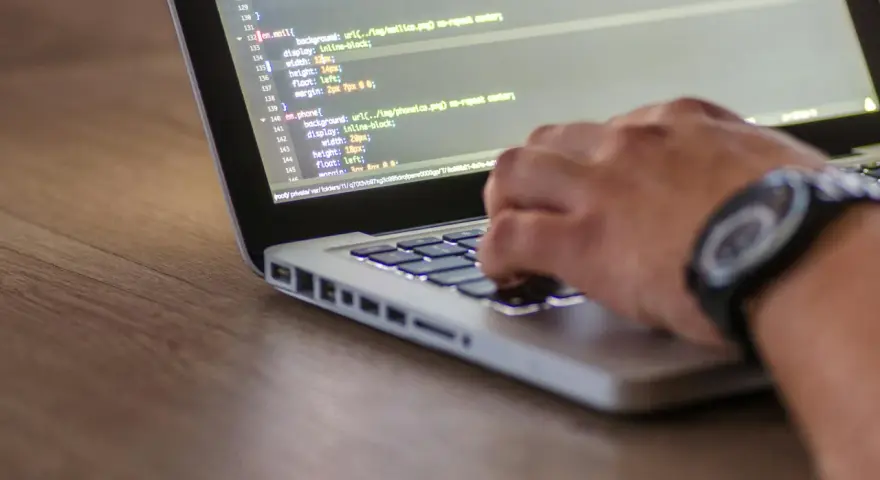 Kodowanie strony internetowej, widać fragment kodu HTML z listą nieuporządkowaną i rękę piszącą na klawiaturze.