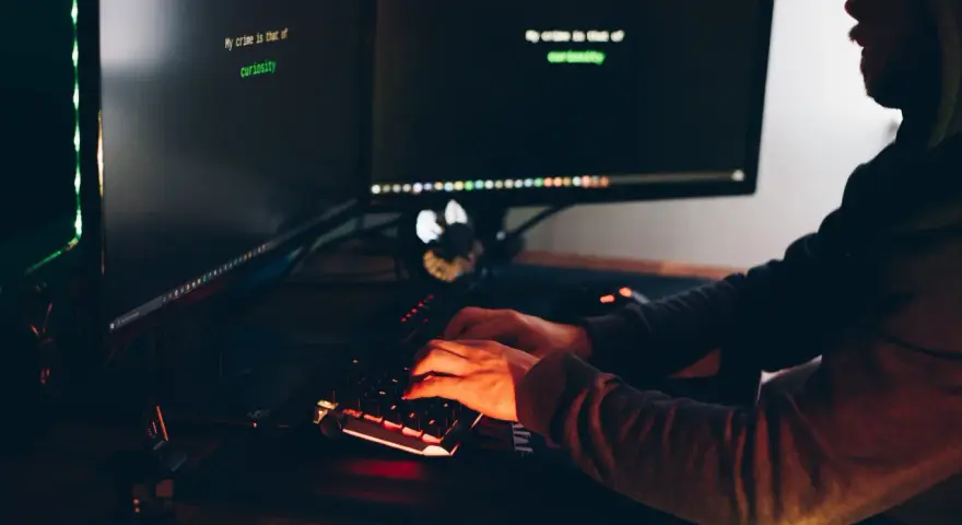 Osoba w kapturze pisze na klawiaturze, na ekranie widać tekst "My crime is that of curiosity". Może szukać **backdoors** w systemie.