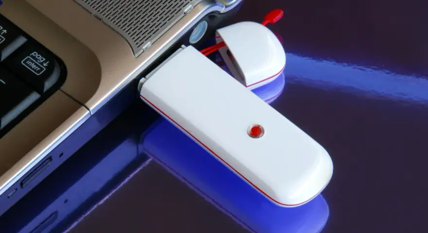 Biały modem USB podłączony do laptopa, umożliwiający komórkową transmisję danych.